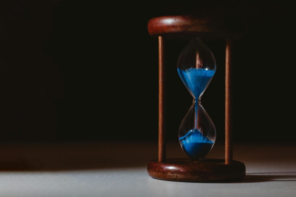 A minimalist close-up of a wooden hourglass with blue sand flowing, symbolizing the passage of time.